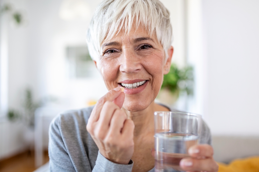 A senior woman taking a vitamin with a glass of water