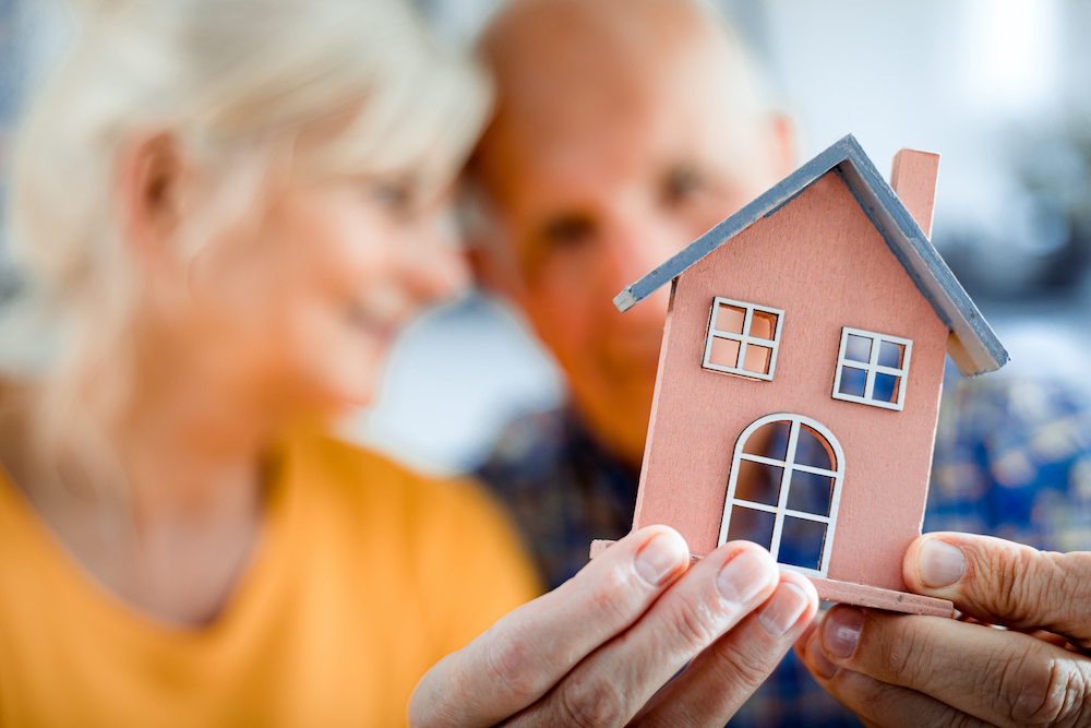 A senior couple holding up a tiny model of a home