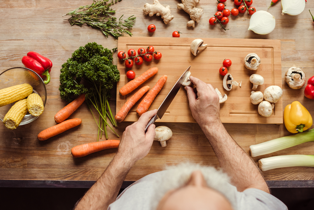 A senior man chops of veggies on a cutting board