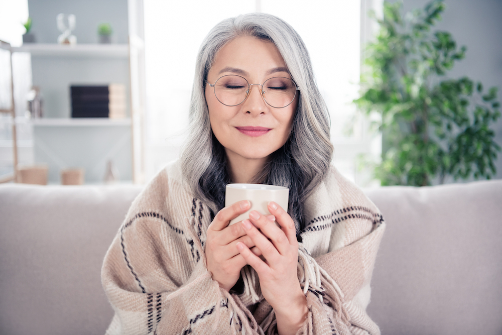 A senior woman sits on the sofa and drinks her tea