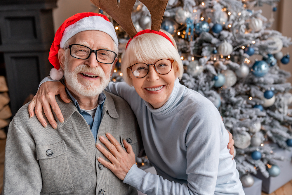 A Madison Heights independent living senior couple sit in front of a Christmas tree