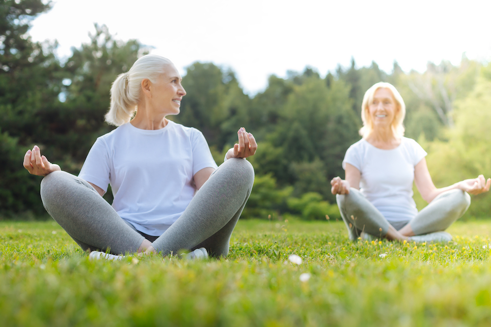Two senior women meditating outdoors at a local park