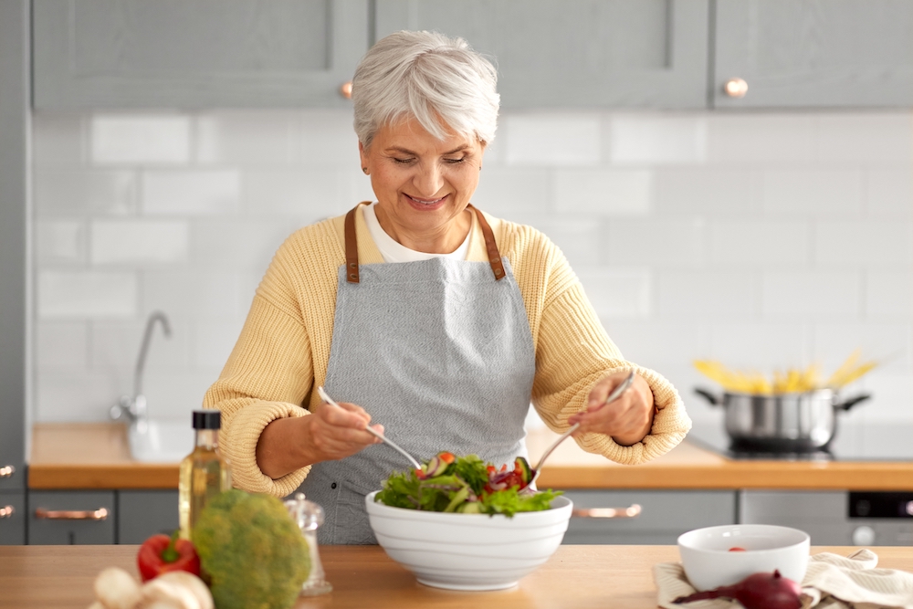 A smiling senior woman prepares a garden salad