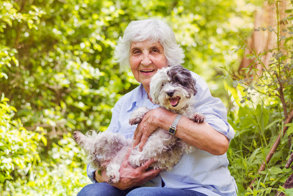 A happy senior woman hugging her small dog while out on a walk