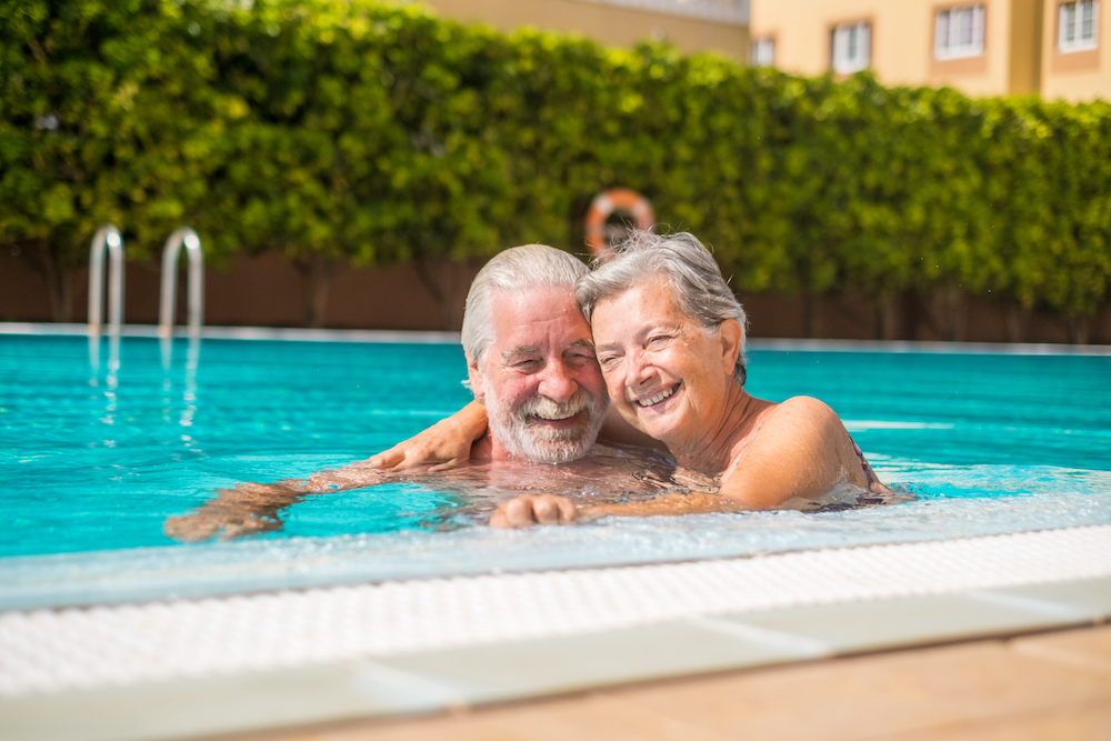 A smiling senior couple enjoy a dip in an outdoor pool during a summer day