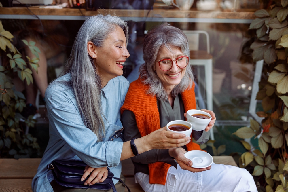 two senior women sitting outside enjoy coffee together