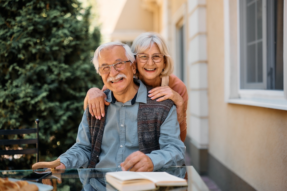 A senior couple hug while sitting on the patio of the Madison Heights senior apartments